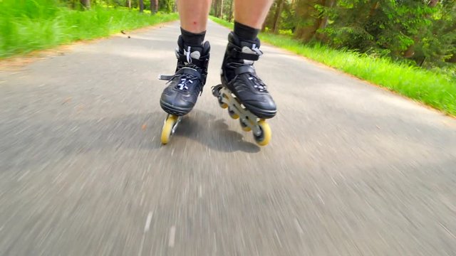 Outdoor shuffle inline skating. Mans legs roller skating on forest asphalt path. Close up view to quick shuffle movement of inline boots.