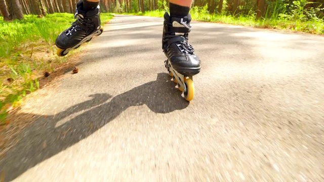 Outdoor shuffle inline skating and t-braking. Mans legs roller skating on forest asphal path. Close up view to quick shuffle movement of inline boots and t-stop with right leg at the end.