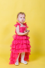 Girl toddler in a pink dress on a yellow background holding a smartphone and looking at the camera