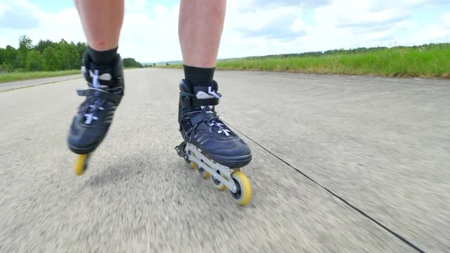 Mans legs roller skating on the asphal. Close up view to quick movement of inline boots.