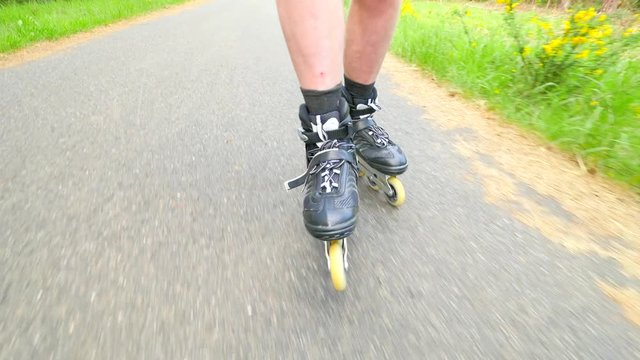 Start inline skating on smooth asphalt in the forest. Close up view to light skin man legs quick movement of inline boots.