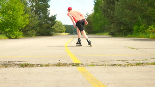 Rear view to inline skater in green running singlet . Outdoor inline skating on smooth asphalt in the forest. Light skin man skating on the road, moving with center of gravity.