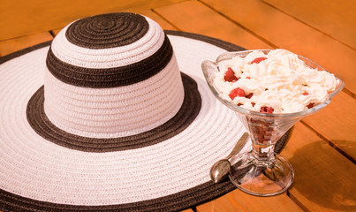 Glass bowl with raspberry and whipped cream and  summer hat. Selective focus