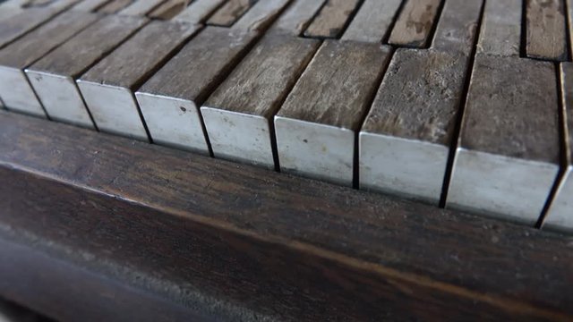 CLOSE UP, DOF: Detail of barely visible human fingers playing antique ruined piano. Hands pushing keys on crumbling keyboard. White and black paint crumbling off the abandoned musical instrument