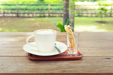 Coffee cup and pastry on wooden table with nature background.