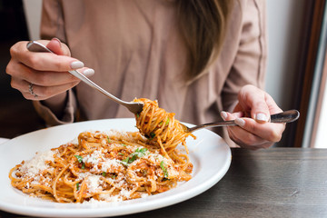 girl eats Italian pasta with tomato, meat. Close-up spaghetti Bolognese wind it around a fork with...