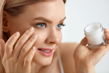 Beauty Woman Face. Girl With Fresh Skin And Cream Bottle In Hand