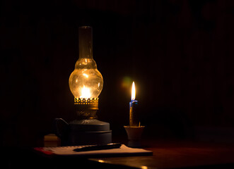 Obraz na płótnie Canvas Kerosene lamp yellow flame and a candle light notebook with pen in a dark room