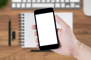 Hand holding smartphone with white blank screen over wood desk table.
