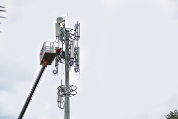 Two workers on crane installing mobile network communication antenna