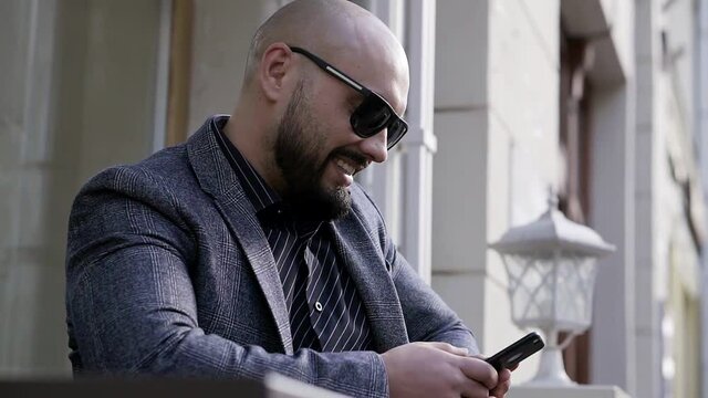 Happy-dressed man businessman sitting at a table in sunglasses and a business suit smiling fun to read on the mobile phone screen