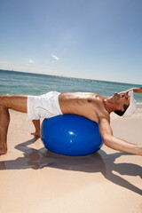 Fototapeta na wymiar homme riant sur la plage avec une balle de gymnastique