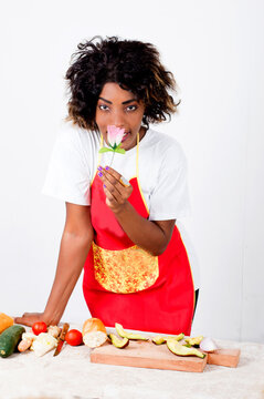 Young woman in a cooking suit holding a flower and before her slices of avocado and vegetables.