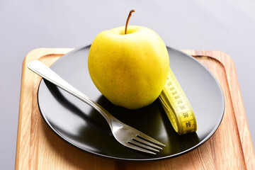 Apple lying on black plate with fork and measuring tape