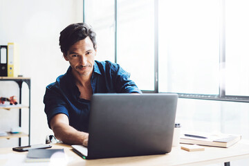 Smiling businessman working on mobile computer at sunny office.Coworker typing on notebook keyboard.Horizontal,blurred background.