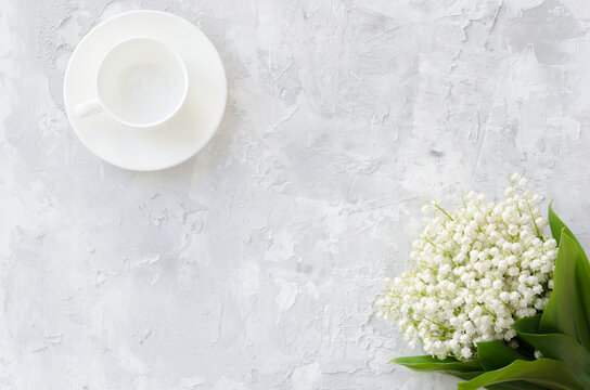 Lily of the valley bouquet and empty cup for coffee on a concrete texture