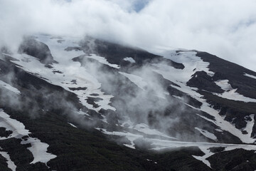 Mountain slopes covered by melting snow and clouds