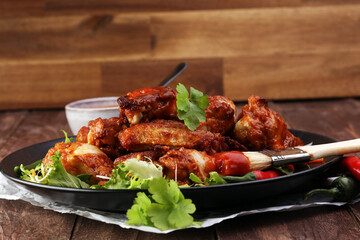 barbecue chicken wings close up on wooden tray with red spice sauce and salad