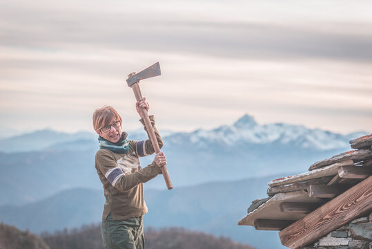 Angry woman holding an axe. Scenic background with mountain peaks, misty valley and moody sky, on the Alps.