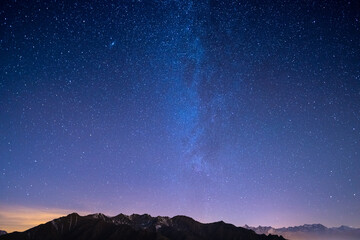 The wonderful starry sky on Christmas time and the majestic high mountain range of the Italian French Alps, with glowing villages below and moonlight.