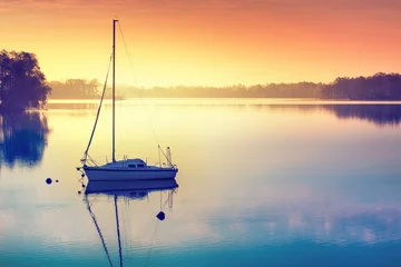 Wandaufkleber Little sailing boat reflects in  the serene water during sunrise. Masuria, Poland. © ysuel