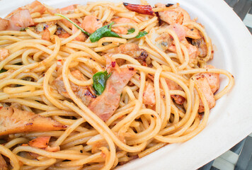 Stir-fried spaghetti with dried chili and bacon on white paper plate