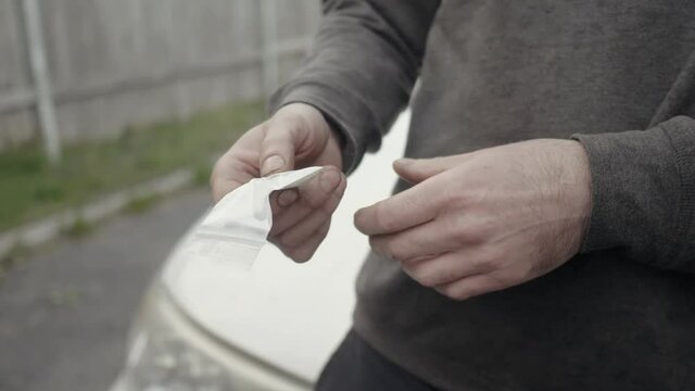 Closeup drug dealer in front of his car trying to sell some cocaine to people passing around.