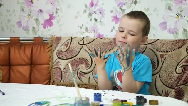 The boy draws paints in the house at the table.