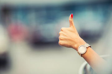 Close-up of a woman hand showing a thumbs-up sign out with car windows. - Powered by Adobe