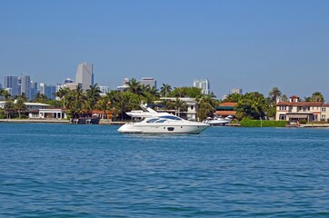 Small white motor yacht idling on the florida intra-coastal waterway with expensive dilido island real estate and the high rise Miami skyline in the background.