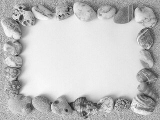Frame of marine pebbles on a white paper on the sand. black and white image