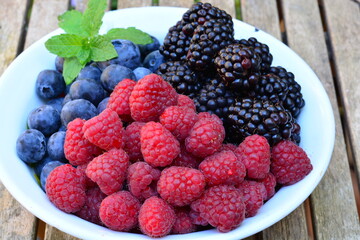 Raspberries, blackberries and blueberries in a bowl on a wooden table