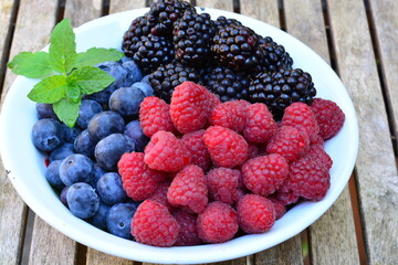 Raspberries, blackberries and blueberries in a bowl on a wooden table