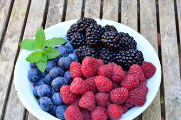 Raspberries, blackberries and blueberries in a bowl on a wooden table
