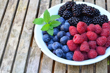 Raspberries, blackberries and blueberries in a bowl on a wooden table