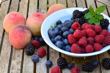 Raspberries, blackberries and blueberries with peaches in a bowl on a wooden table