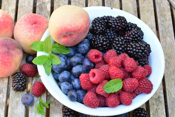 Raspberries, blackberries and blueberries with peaches in a bowl on a wooden table