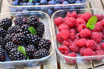 Raspberries, blackberries and blueberries in a plastic box on a wooden table
