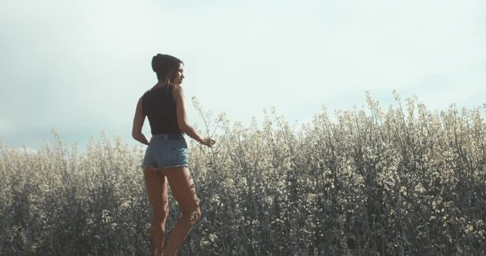 Young attractive female walking on a rural road near rapeseed field. 4K UHD RAW edited footage