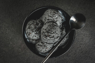 Trendy food. Black ice cream with black sesame, in a black bowl on a black stone table, with a spoon. Copy space top view