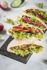 Snack. Takeaway food, street fast food. Pita bread sandwich with fresh vegetables lettuce, cucumber, tomato, radish, beef meat. On a light concrete table on a wooden tray. Copy space