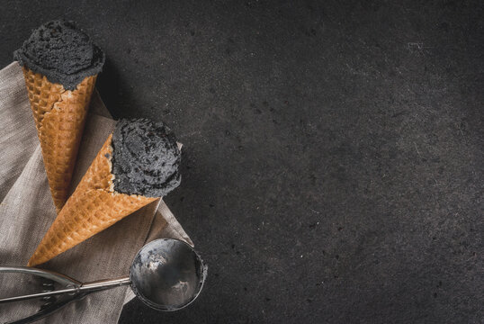 Trendy food. Black ice cream with black sesame, in traditional portioned ice cream cones. On a black stone table, in a wooden tray. Copy space top view