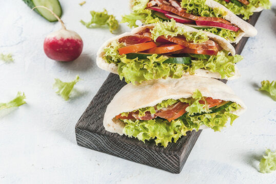 Snack. Takeaway food, street fast food. Pita bread sandwich with fresh vegetables lettuce, cucumber, tomato, radish, beef meat. On a light concrete table on a wooden tray. Copy space
