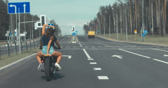Couple travel on a custom built cafe racer motorcycle on a highway. Girls hugs a guy. 4K UHD RAW edited footag