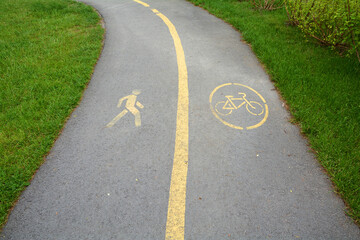 Obraz premium The sidewalk and bike path. Yellow bicycle sign on asphalt bike lane on city park in background.