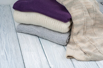 Knitted wool sweaters. Pile of knitted winter clothes on wooden background, sweaters, knitwear, space for text.