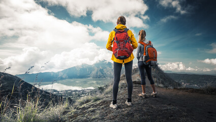 Two hikers stand on the top of a mountain and enjoy valley view