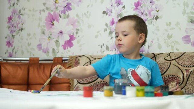 The boy draws paints in the house at the table.