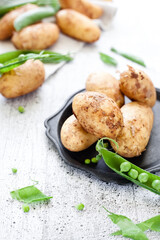 New season raw potatoes with green peas on white wooden background