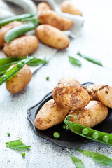 New season raw potatoes with green peas on white wooden background